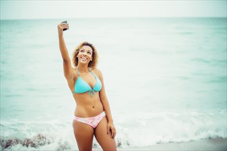 Mixed race teenager taking selfie in bikini on beach