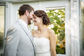 Caucasian bride and groom touching foreheads in garden