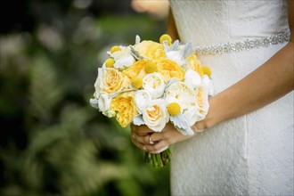 Caucasian bride holding bouquet in garden