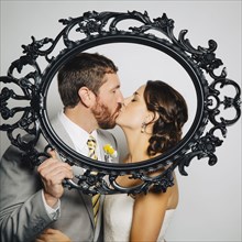 Caucasian bride and groom kissing behind empty frame