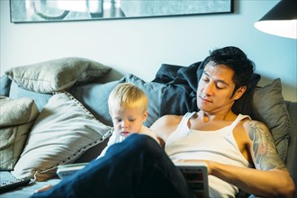 Father and son reading on sofa in living room