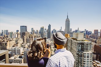 Indian couple taking cell phone photograph of New York cityscape