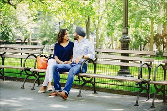 Indian couple sitting on bench in urban park