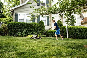 Caucasian boy mowing front lawn
