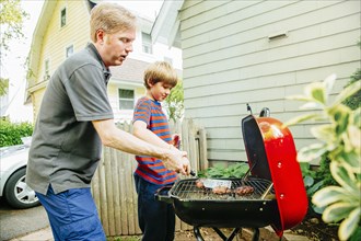 Caucasian father and son grilling food in backyard
