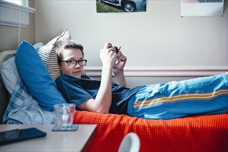 Caucasian boy using cell phone on bed