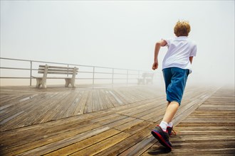 Caucasian boy running on wooden boardwalk