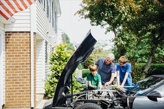 Caucasian grandfather and grandsons repairing car in driveway