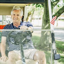 Older Caucasian man driving golf cart