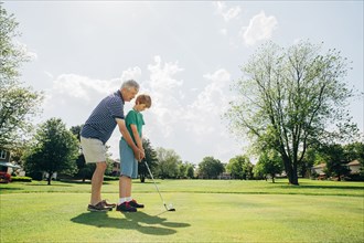 Caucasian grandfather teaching grandson golf on course