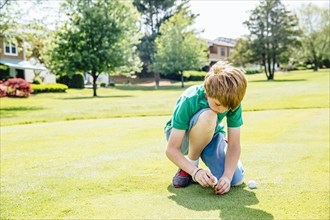 Caucasian boy setting up golf ball on course