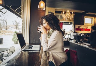 Woman using laptop and drinking coffee in cafe