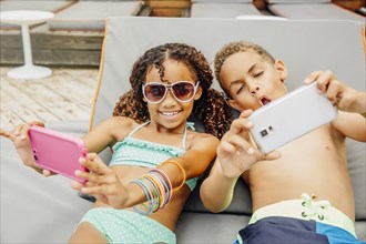 Mixed race children taking selfie with cell phones on patio