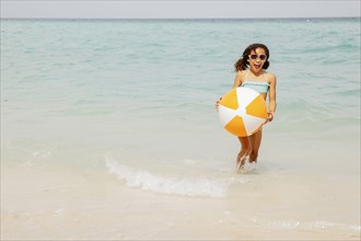 Mixed race girl holding beach ball in ocean waves