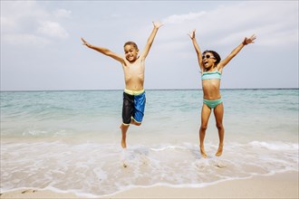 Mixed race children jumping for joy on beach