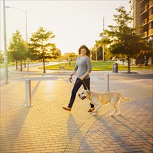 Caucasian woman walking dog on sidewalk
