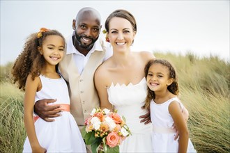 Newlywed couple and daughters smiling outdoors
