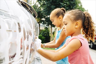 Mixed race sisters washing car