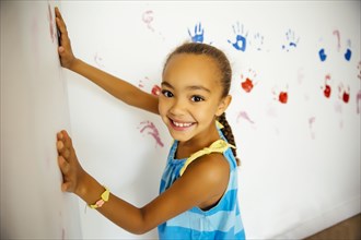 Mixed race girl making hand prints on wall