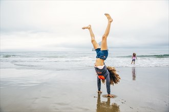 Mixed race girl doing handstand on beach