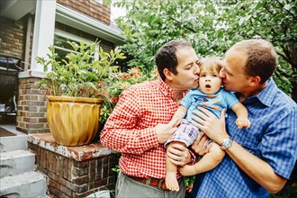 Gay fathers kissing baby son outdoors