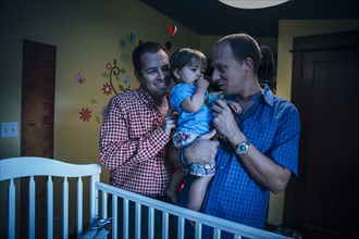 Gay fathers holding baby son in nursery