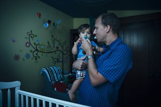 Father giving baby son pacifier in nursery