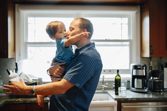 Father kissing baby son in kitchen