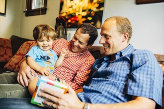 Gay fathers playing with baby son on sofa
