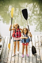 Mixed race sisters holding oars at lake