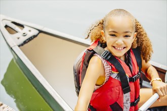 Mixed race girl smiling in canoe in lake