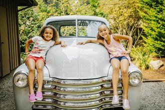 Mixed race sisters sitting on vintage car