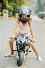 Mixed race girl sitting on miniature motorcycle