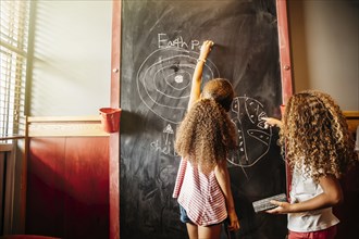 Mixed race sisters drawing on chalkboard