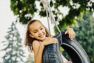 Mixed race girl smiling in tire swing