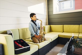 Mixed race boy playing saxophone on sofa