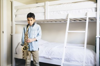 Mixed race boy playing saxophone in bedroom