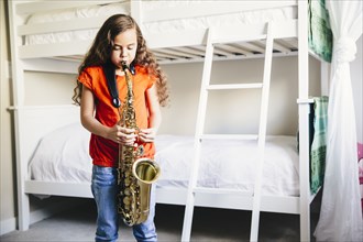 Mixed race girl playing saxophone in bedroom