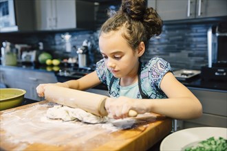 Mixed race girl rolling dough in kitchen