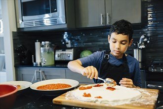 Mixed race boy making pizza in kitchen