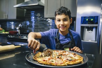 Mixed race boy slicing pizza in kitchen