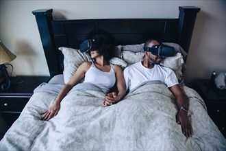 Couple using virtual reality goggles in bed