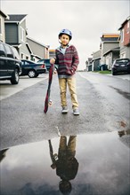 Mixed race boy with skateboard reflected in puddle