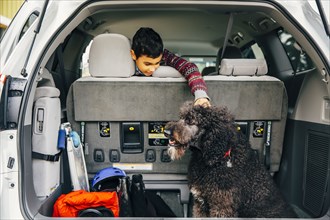 Mixed race boy petting dog in car hatch