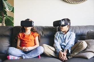 Mixed race children using virtual reality goggles on sofa