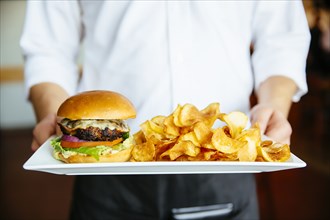 Caucasian waiter holding plate of cheeseburger and chips