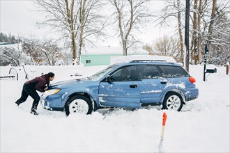 Caucasian woman pushing car stuck in snow