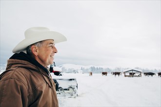 Caucasian farmer admiring cows in snowy field
