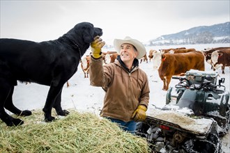 Caucasian farmer petting dog in snowy field