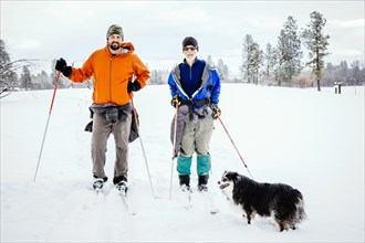 Caucasian couple and dog cross-country skiing in snowy field